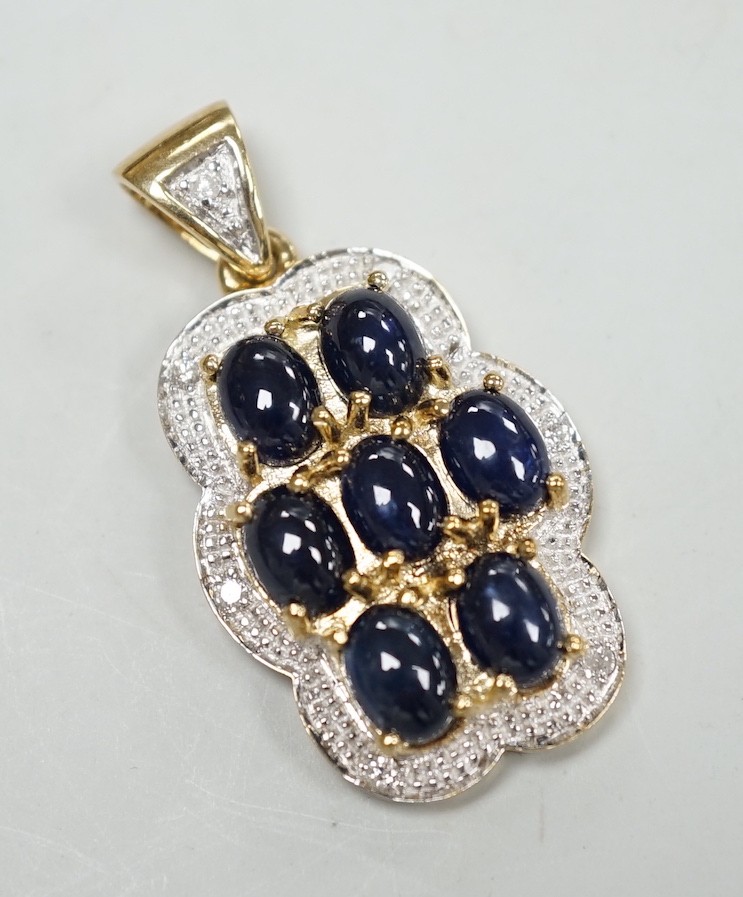 A modern 9ct gold, cabochon sapphire cluster and diamond chip set shaped oval pendant, overall 37mm, gross weight 8.4 grams.